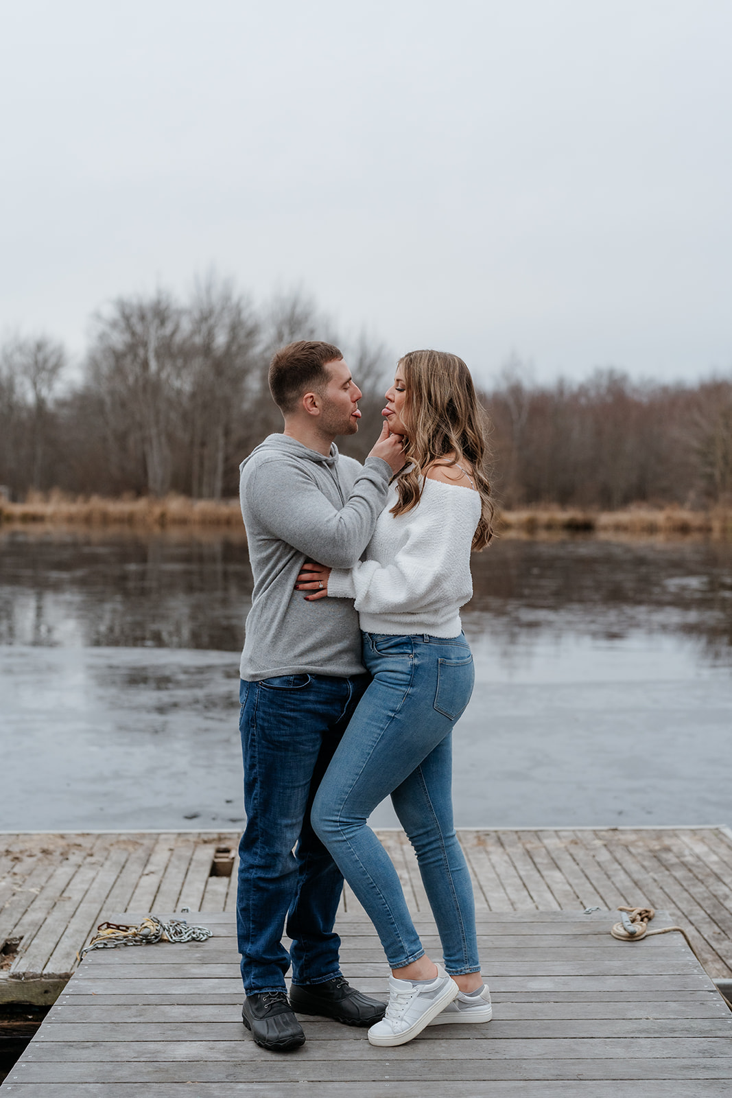 An engaged couple standing on a dock next to a lake.