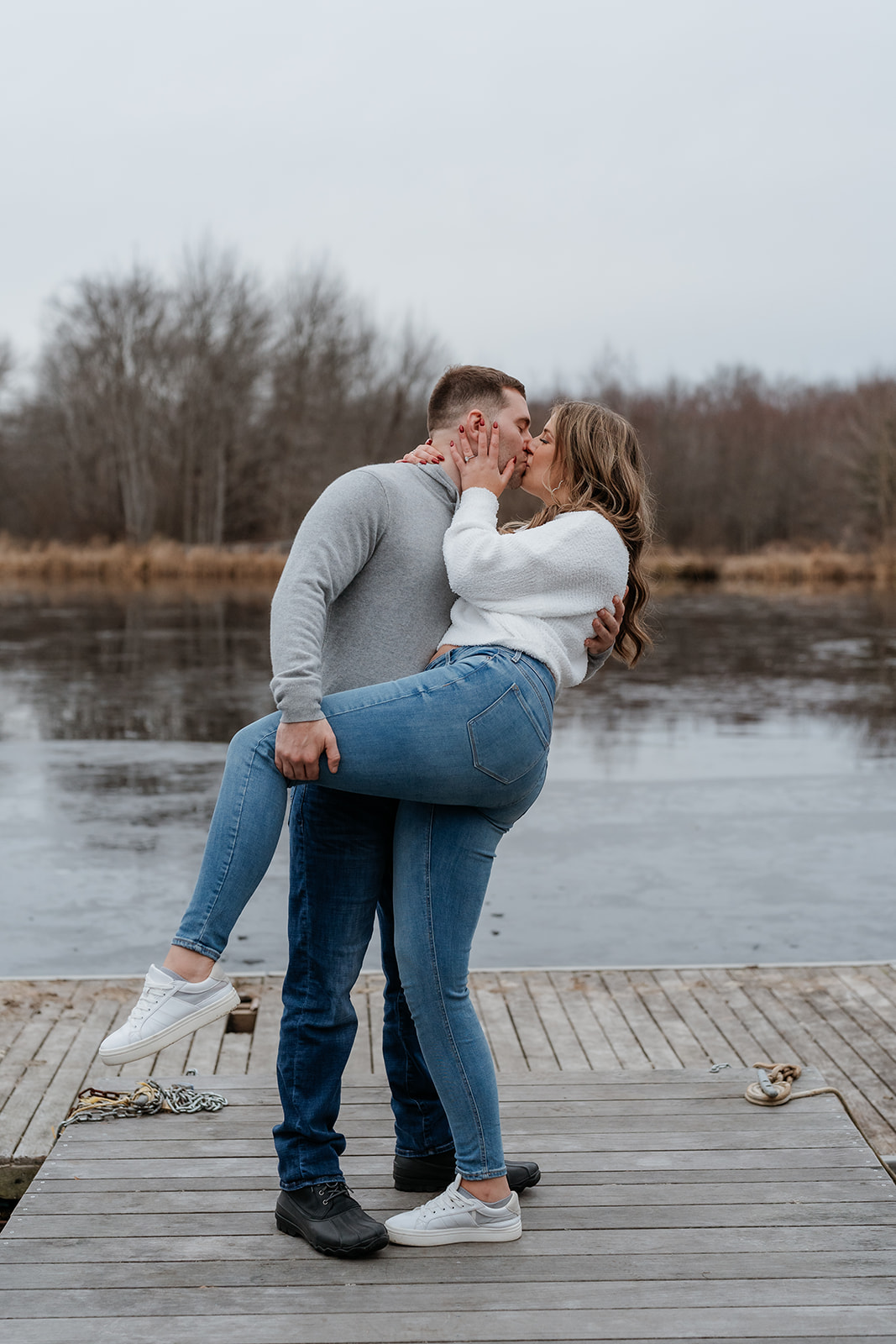 An engaged couple standing on a dock next to a lake.