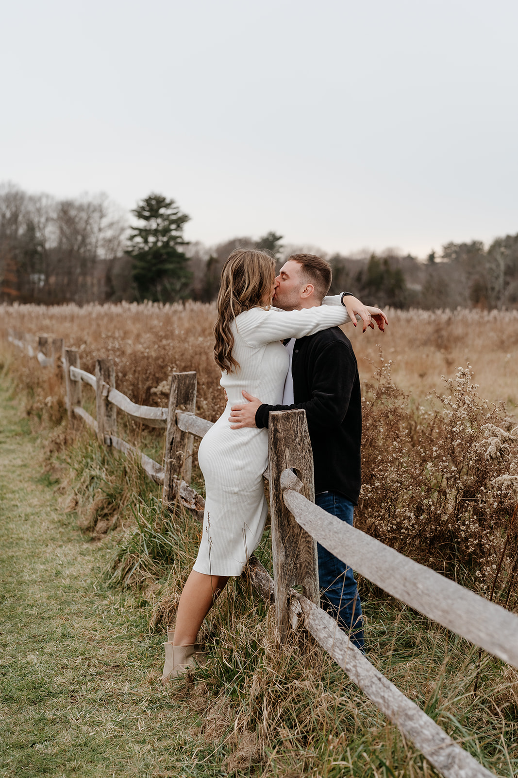 A man and woman kissing on a fence at Powers Farm during their documentary engagement session.