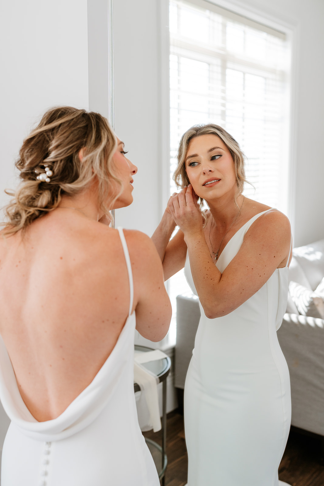 Bride getting ready and looking into mirror while putting on her earrings