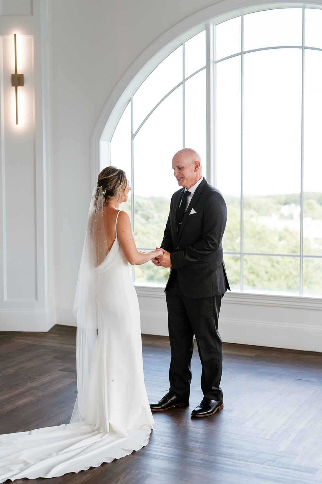Bride and dad holding hands in front of a big window