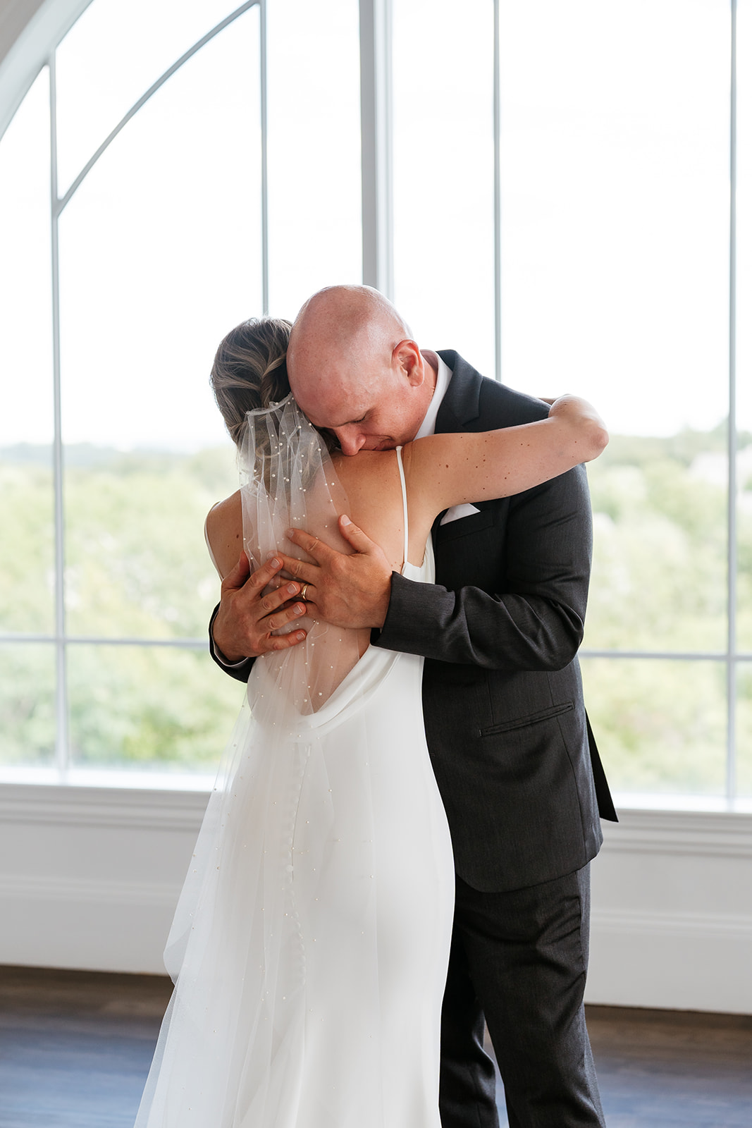 bride and dad hugging in front of a large window