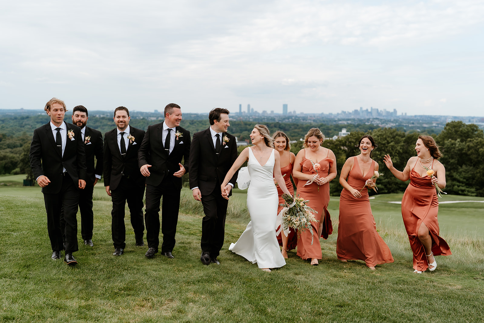 Wedding party celebrating against Boston skyline. Bridesmaids and groomsmen buzzing with excitement and joy.
