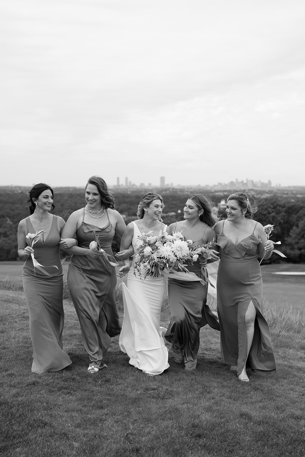 Wedding party celebrating against Boston skyline. Bridesmaids and groomsmen buzzing with excitement and joy.