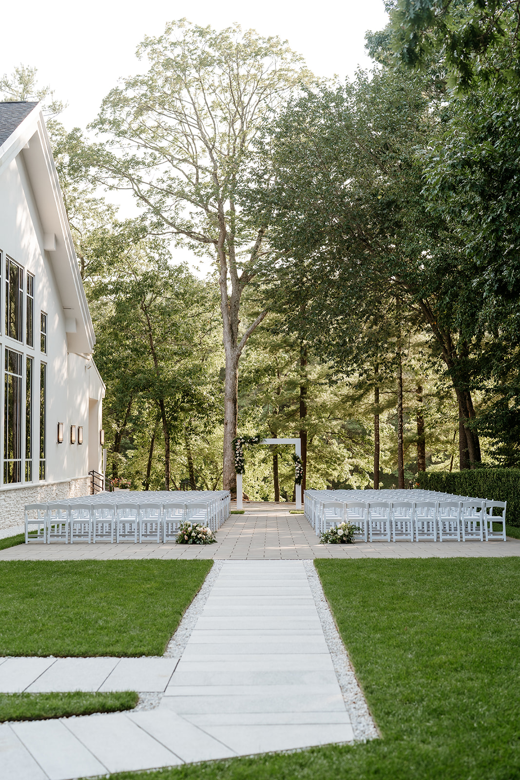 Outdoor wedding ceremony setup with white chairs lined along a pathway leading to an arch in a serene garden setting at Lakeview Pavilion