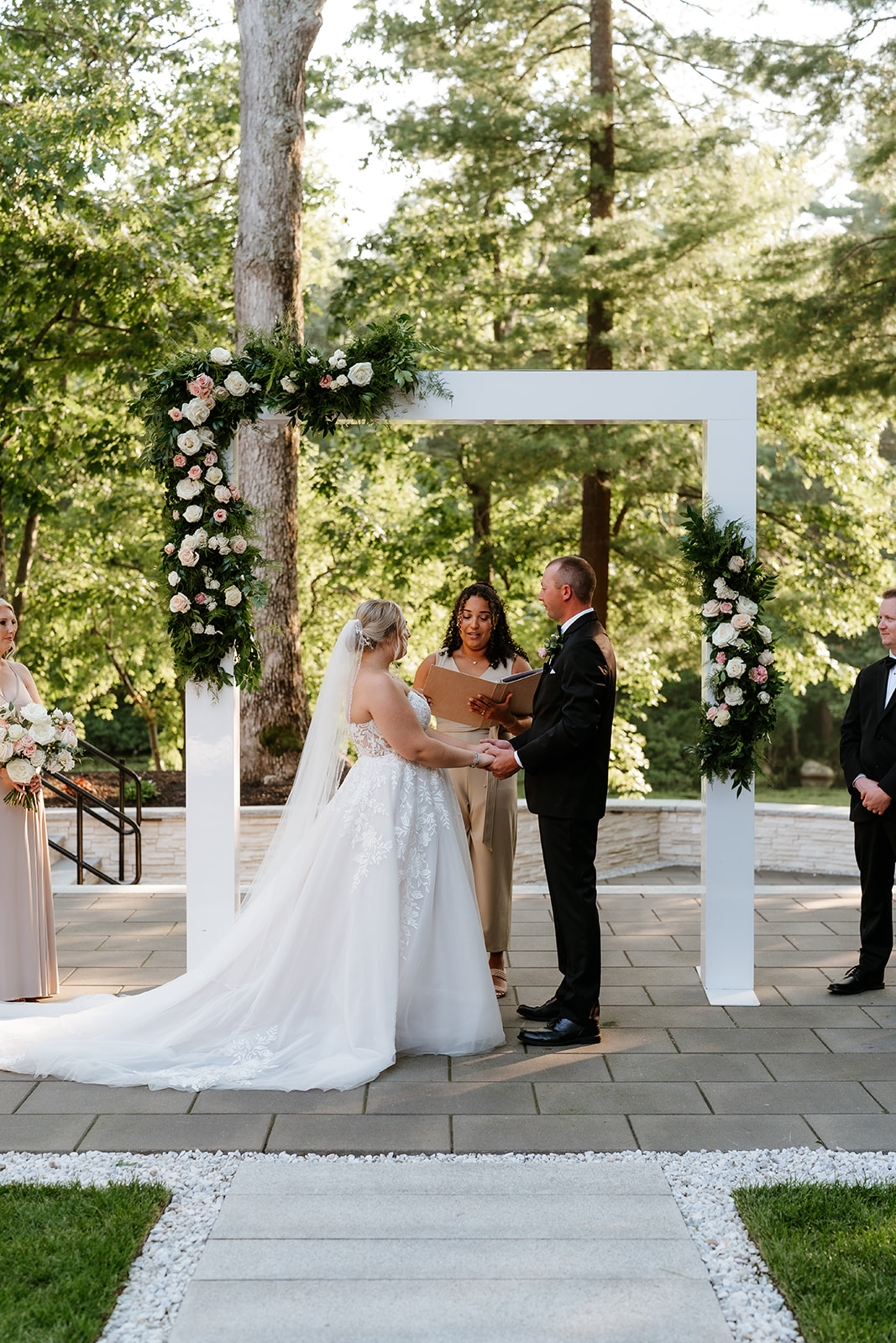 A bride and groom hold hands at an outdoor wedding ceremony while surrounded by their bridal party at Lakeview Pavilion.