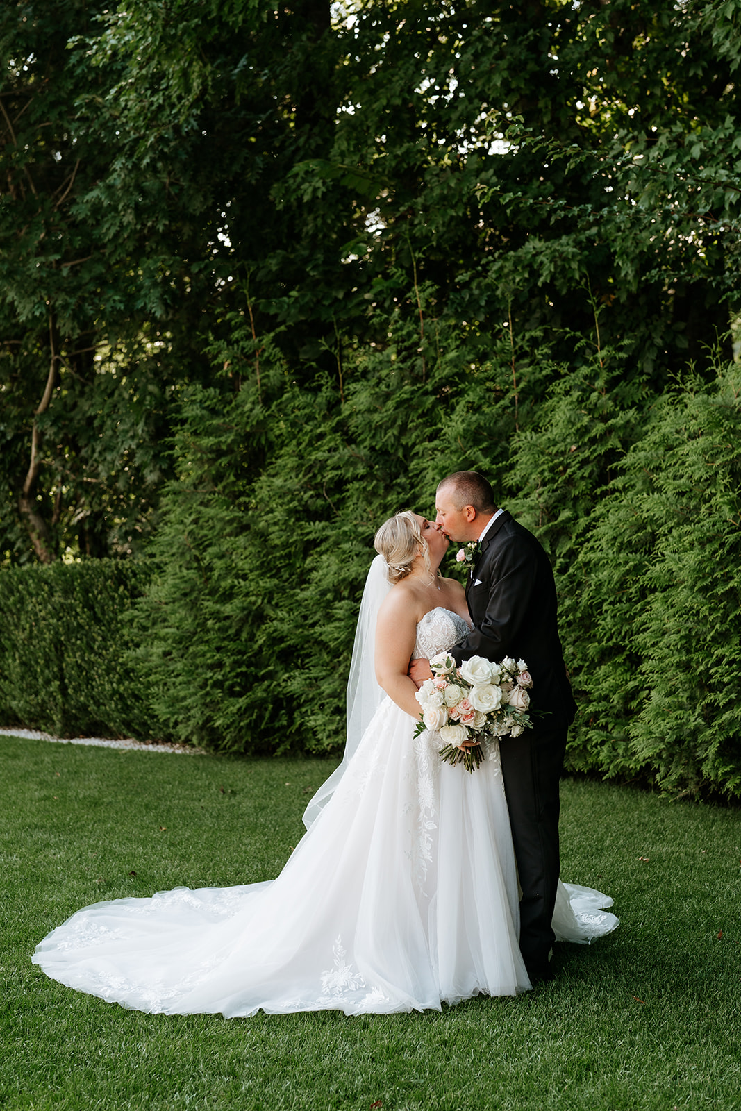 A bride and groom sharing their first look at Lakeview Pavilion in an outdoor setting with tall hedge trees in the background. 