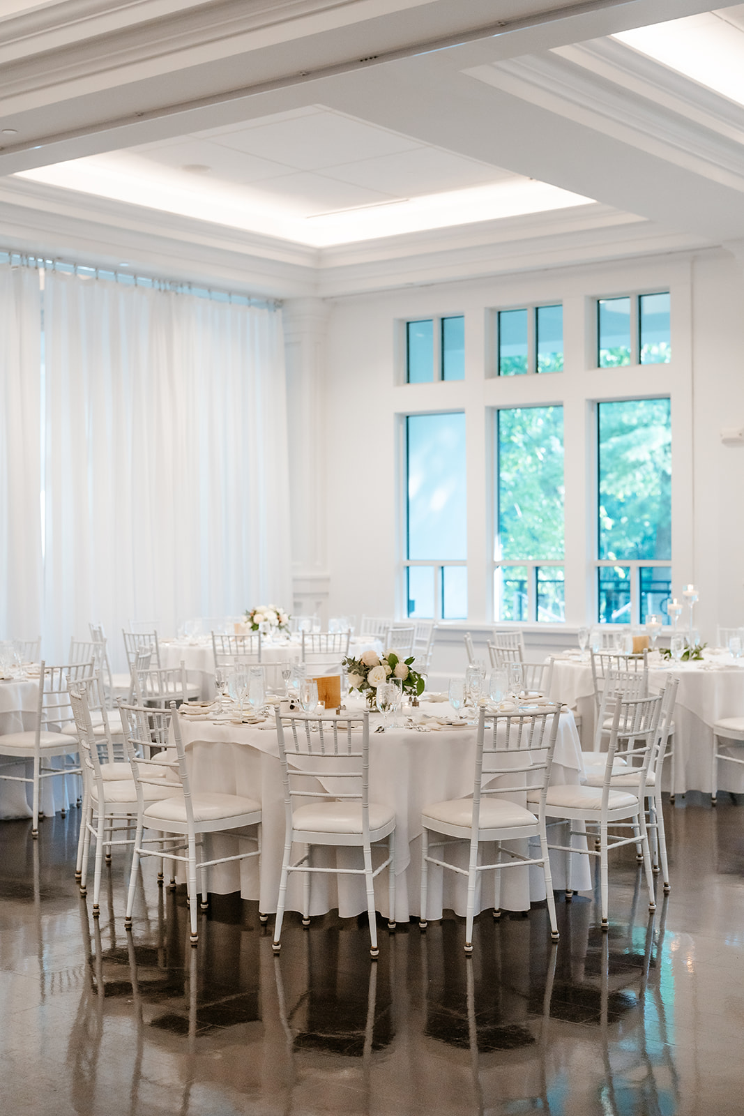 Elegant dining setup in a bright banquet hall with white decor and natural light.