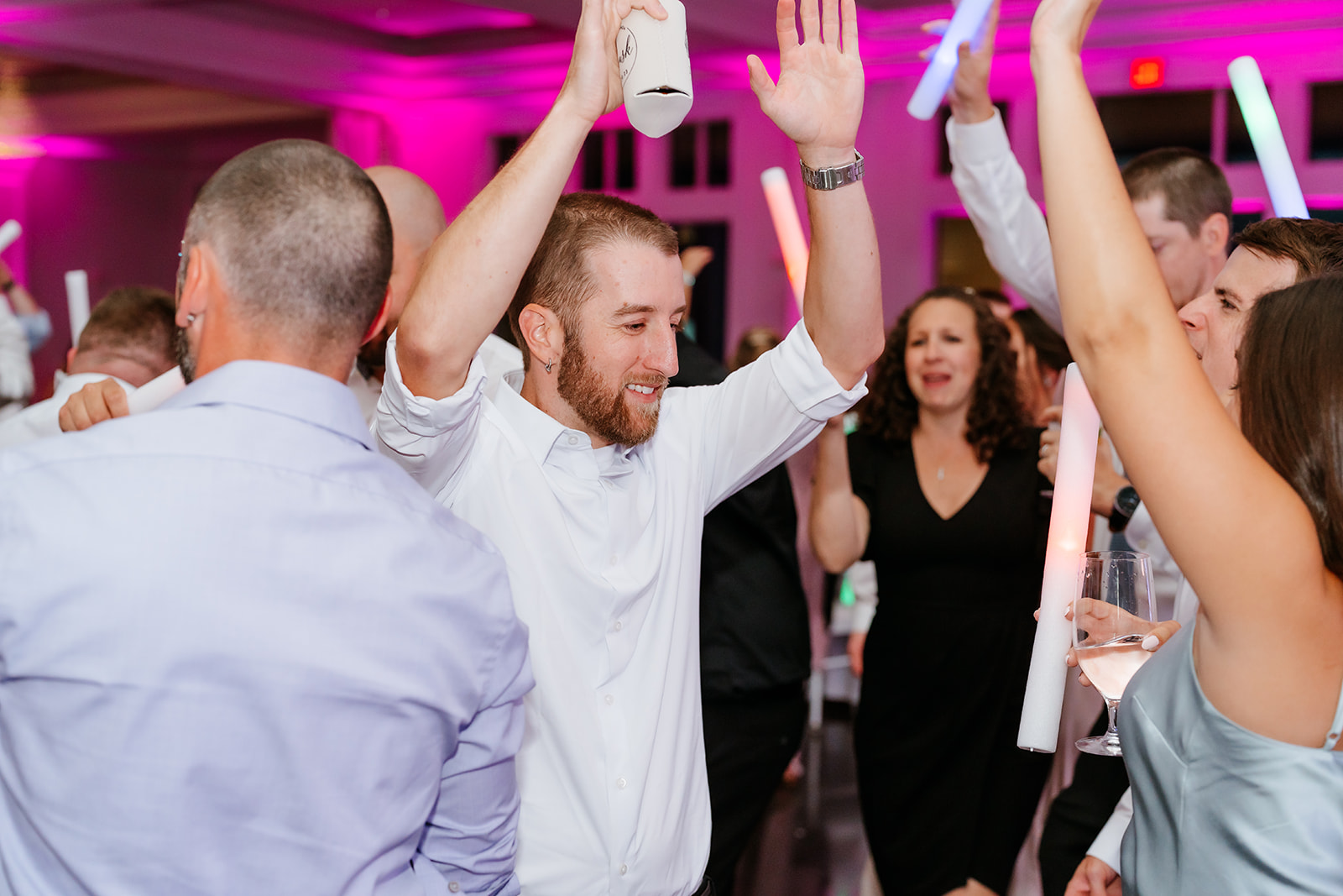 Group of people enjoying a lively celebration with high-fives and dancing in a room with pink lighting.