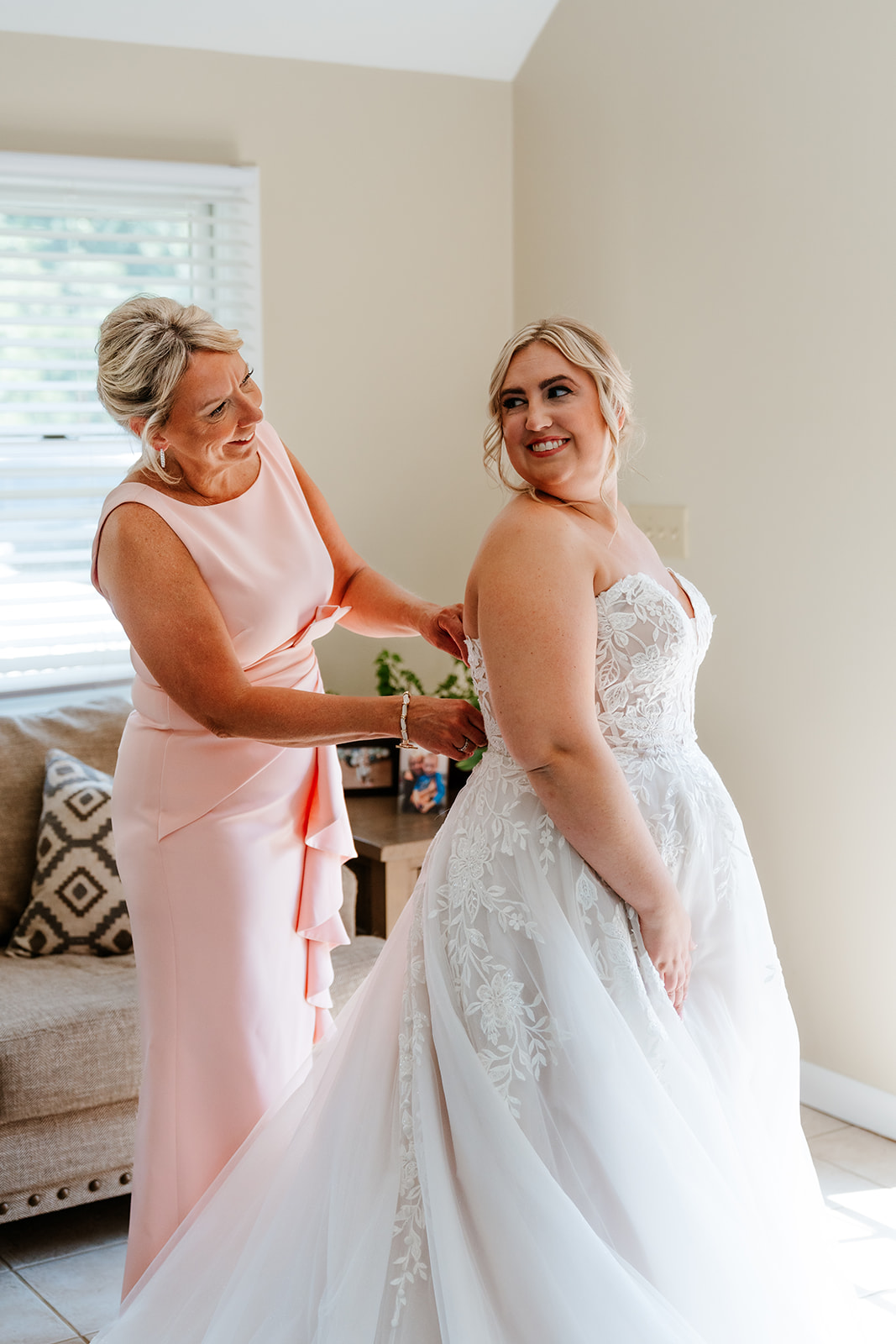 A woman in a peach dress assisting a bride in a white wedding gown, preparing for a wedding ceremony at lakeview pavilion