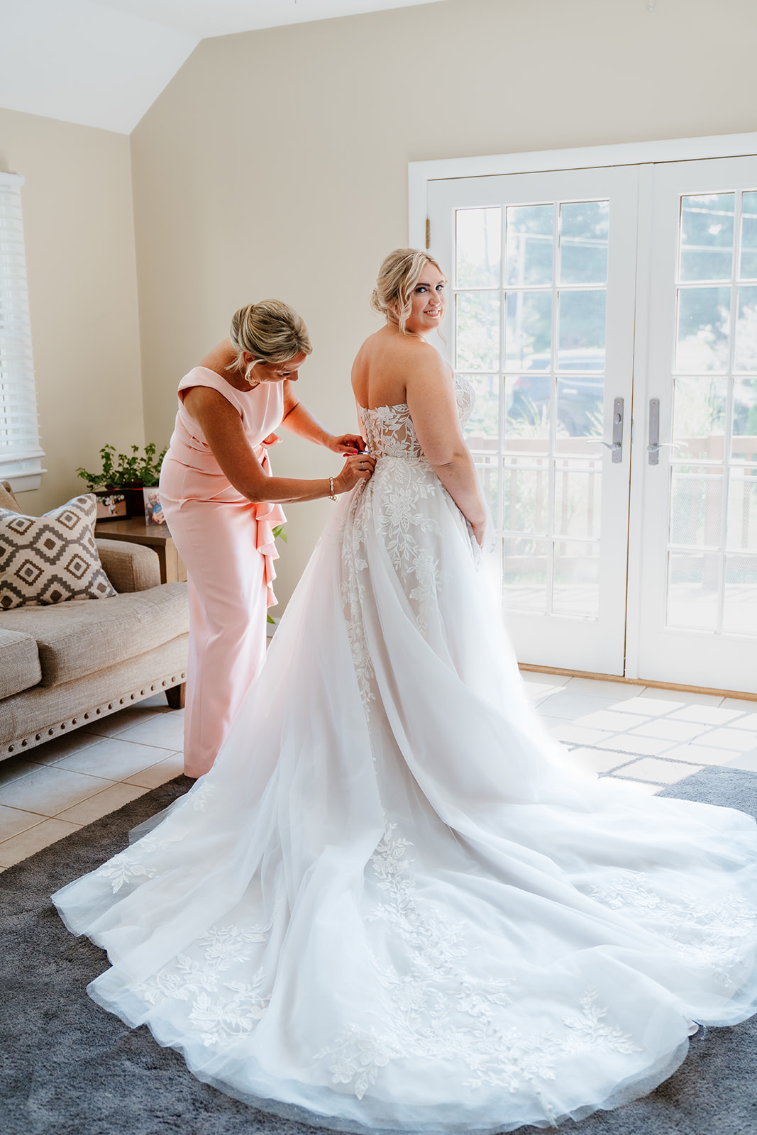 A woman in a peach dress assisting a bride in a white wedding gown, preparing for a wedding ceremony at lakeview pavilion