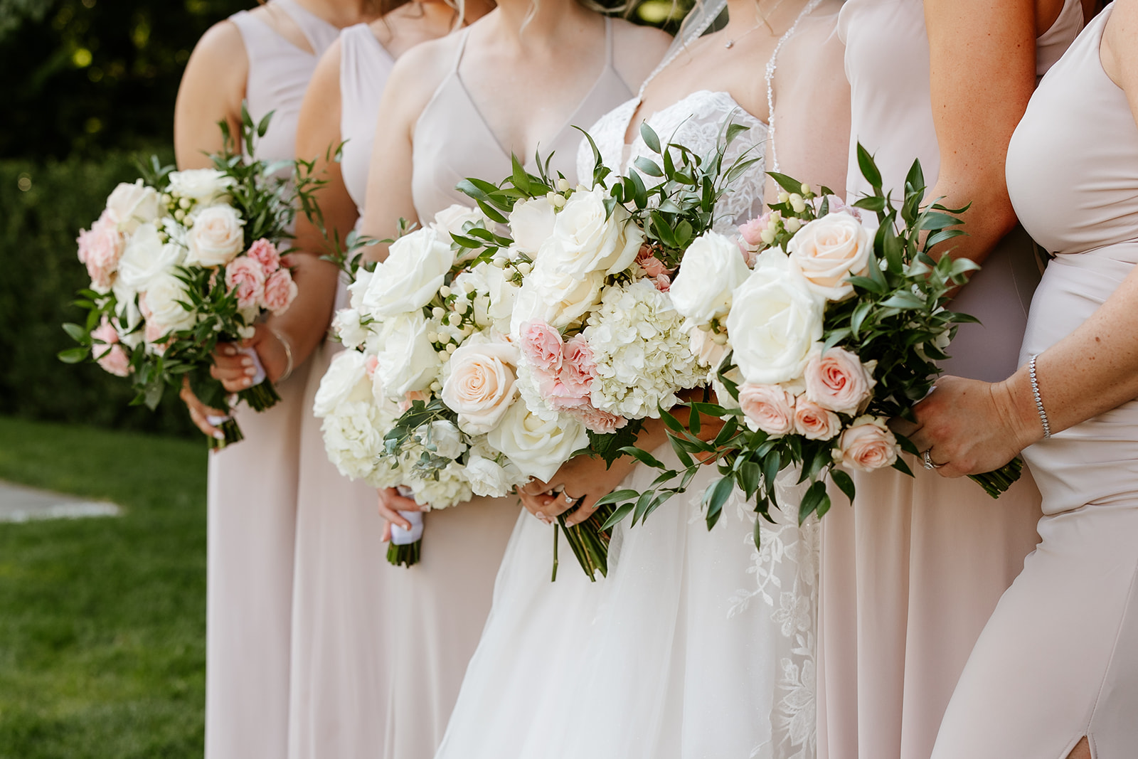 Bridesmaids coordinating dresses pose with a bride, holding bouquets against a backdrop of greenery at Lakeview Pavilion