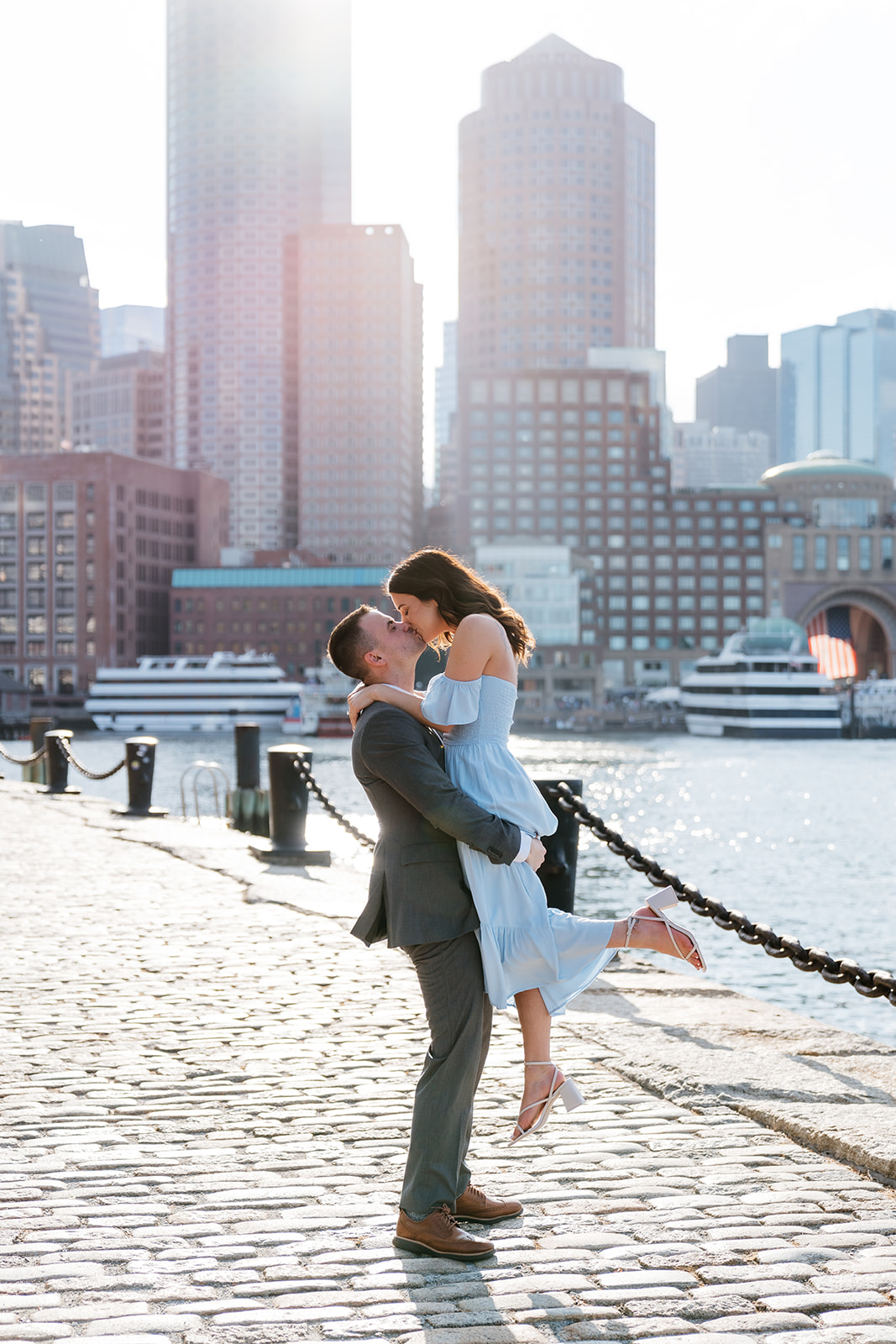 Couple embracing on a city waterfront with skyscrapers in the background at fan pier park as they take Boston engagement photos
