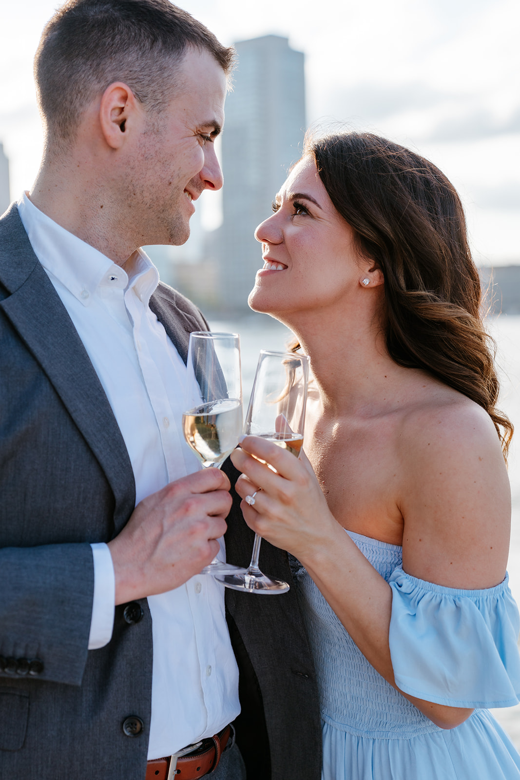A couple toasting with glasses of wine, looking at each other affectionately as they take Boston engagement photos