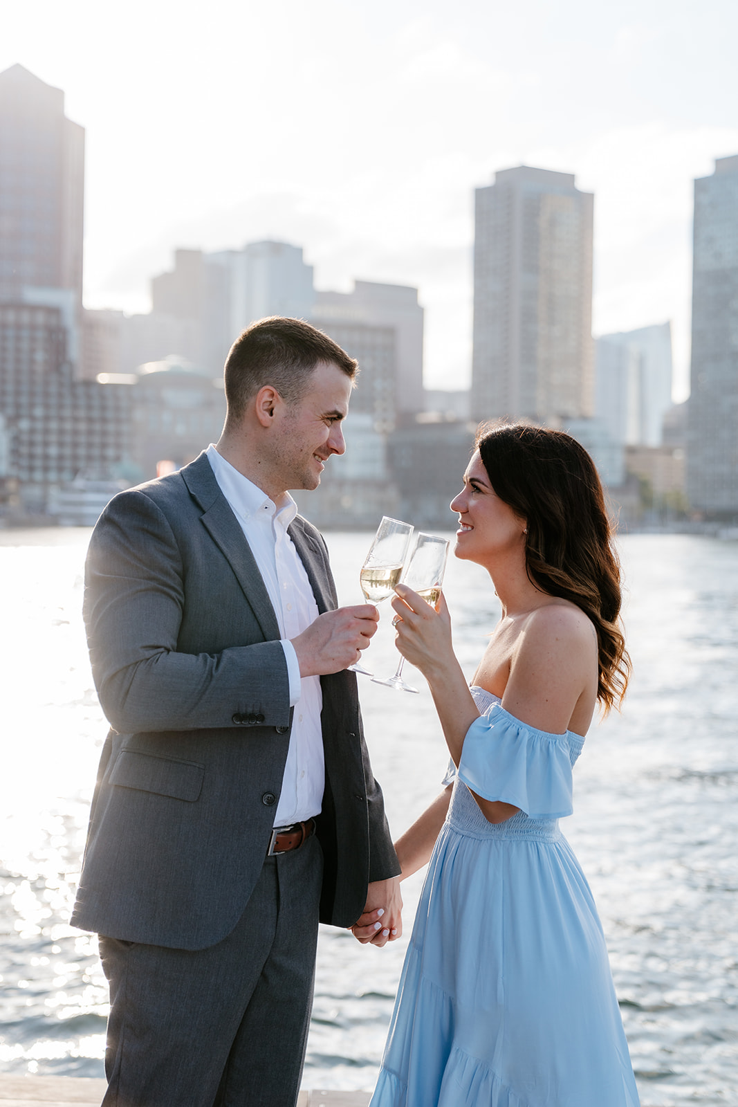 A couple toasting with glasses of wine, looking at each other affectionately as they take Boston engagement photos