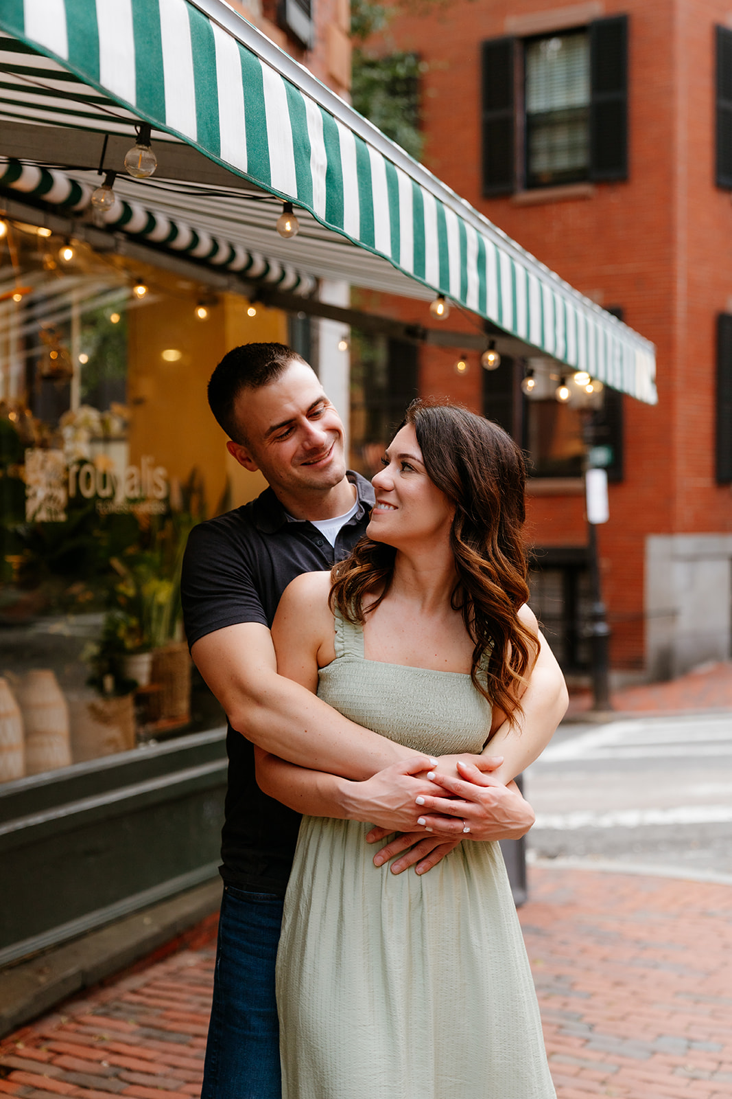 A couple embracing and smiling at each other on the streets of Beacon Hill as they take Boston engagement photos