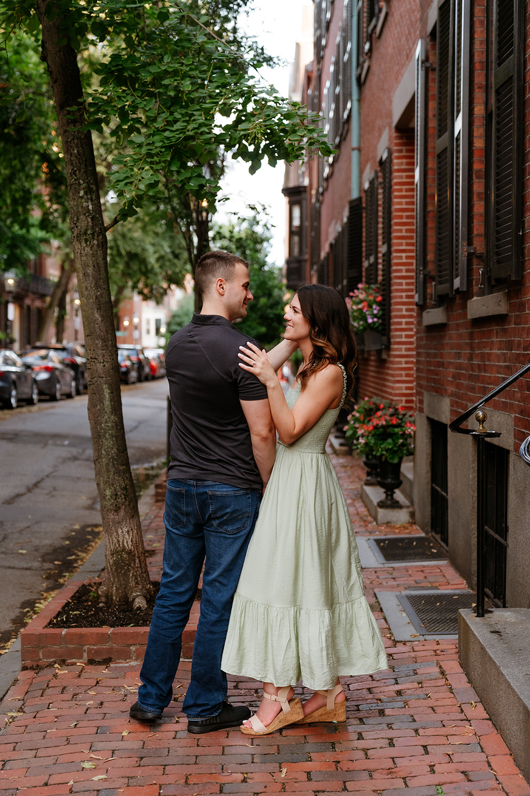 A couple embracing and smiling at each other on the streets of Beacon Hill as they take Boston engagement photos
