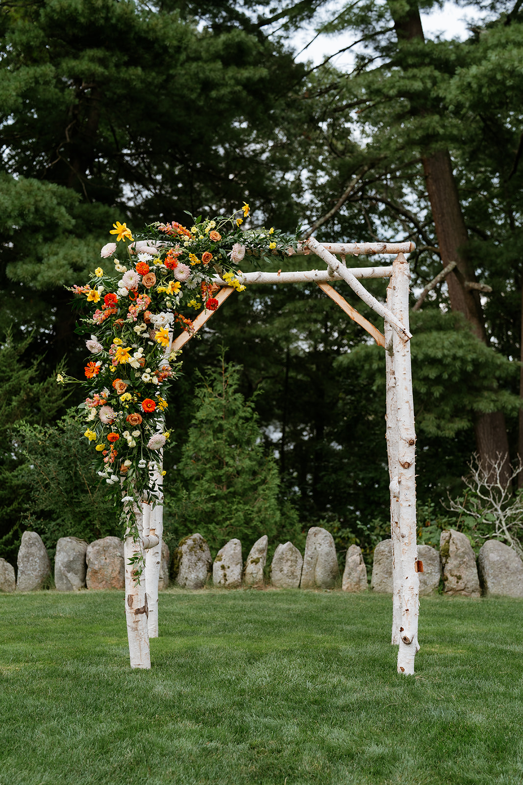Outdoor wedding ceremony setup with white chairs and a floral arch against a backdrop of trees.