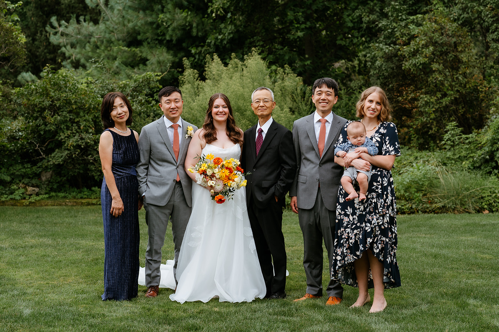 A family posing together at a wedding, featuring a bride holding a bouquet, flanked by older relatives, a man, and a woman holding a baby.