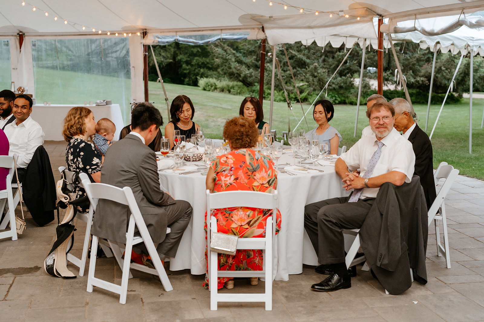 Guests seated at tables during an outdoor tented event, with one man looking towards the camera.