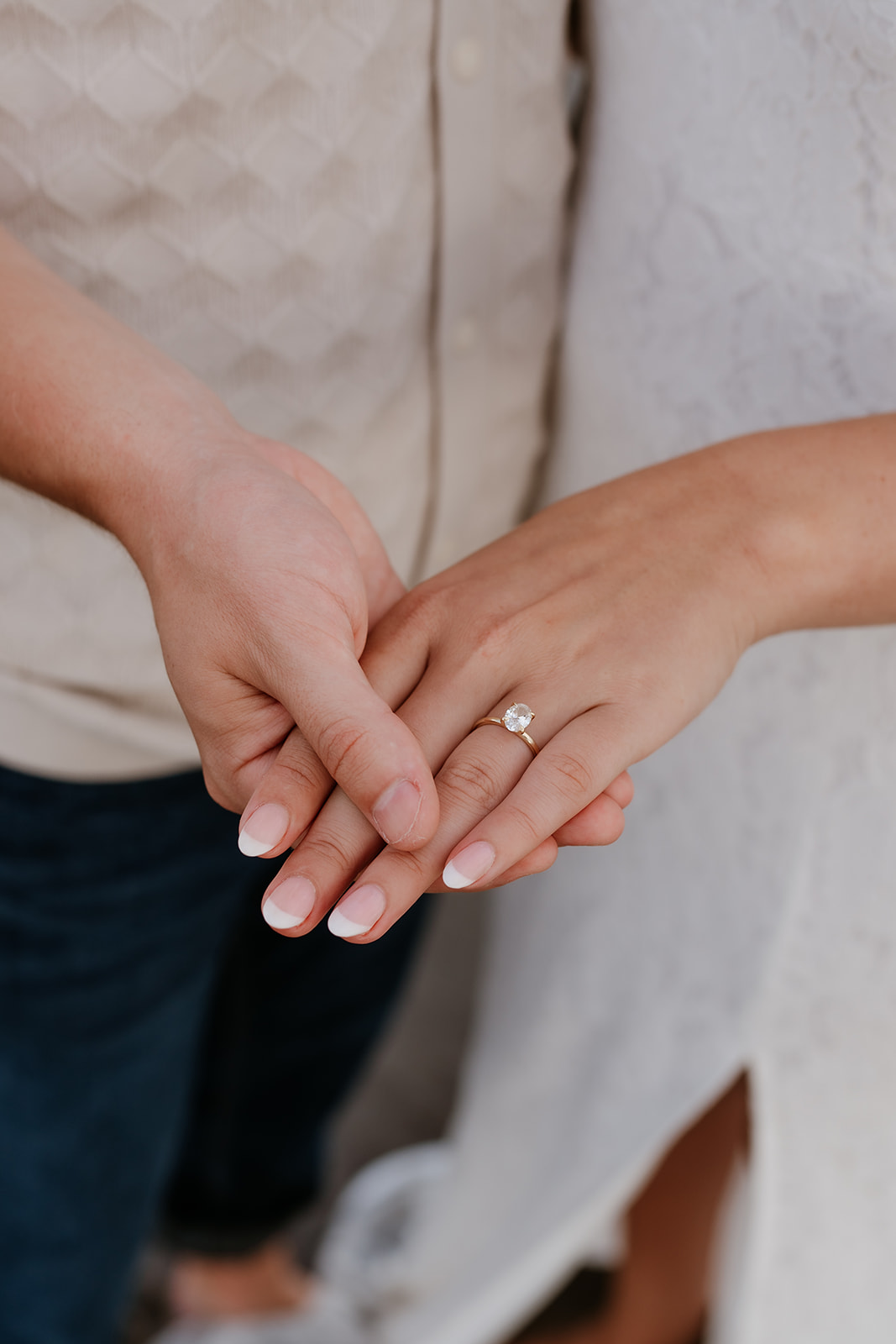 Close-up of a couple holding hands, showcasing an engagement ring on a woman's finger.