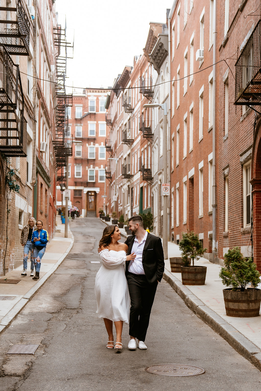 A couple embraces in a cobblestone street surrounded by red brick buildings in North End for their Engagement photos in Boston