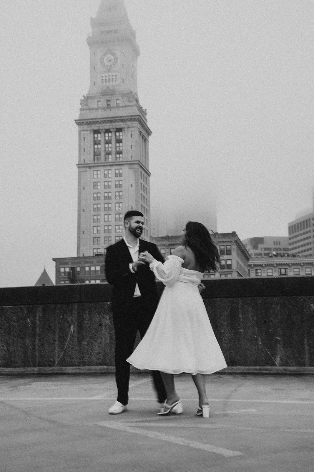 A couple stands on a rooftop parking garage in formal attire;Buildings and a foggy sky are visible in the background