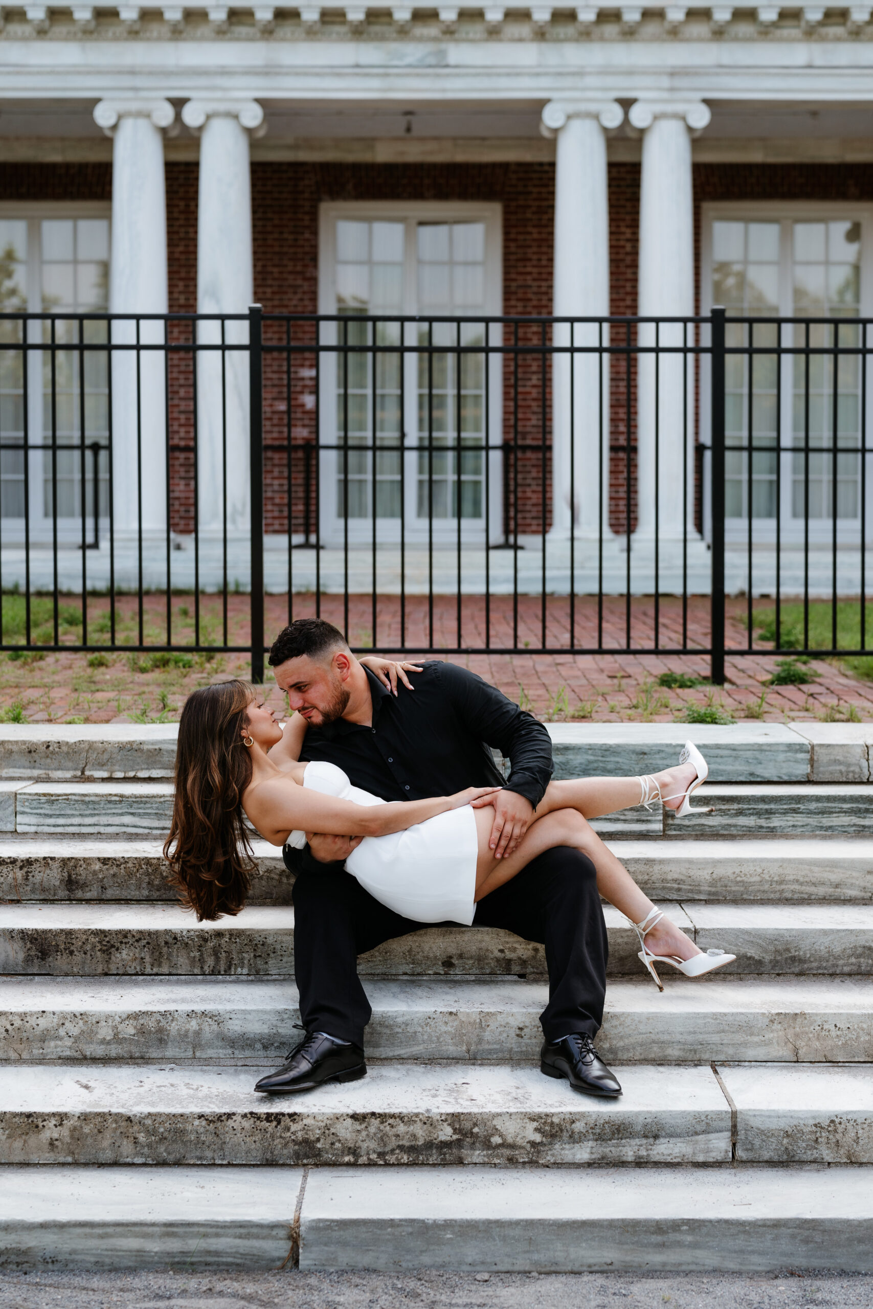 Newly engaged couple sitting on stairs gazing into eachothers eyes during their The Garden at Elm Bank Engagement Session