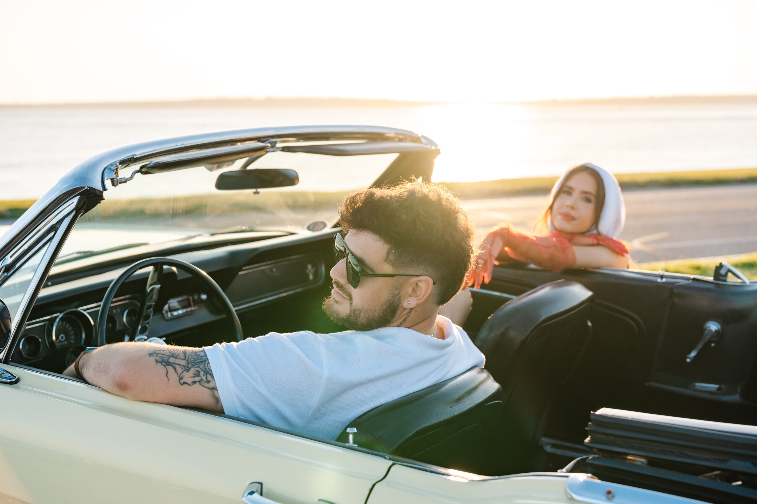 Fiance driving a classic car while soon to be wife is standing outside of the car during sunset