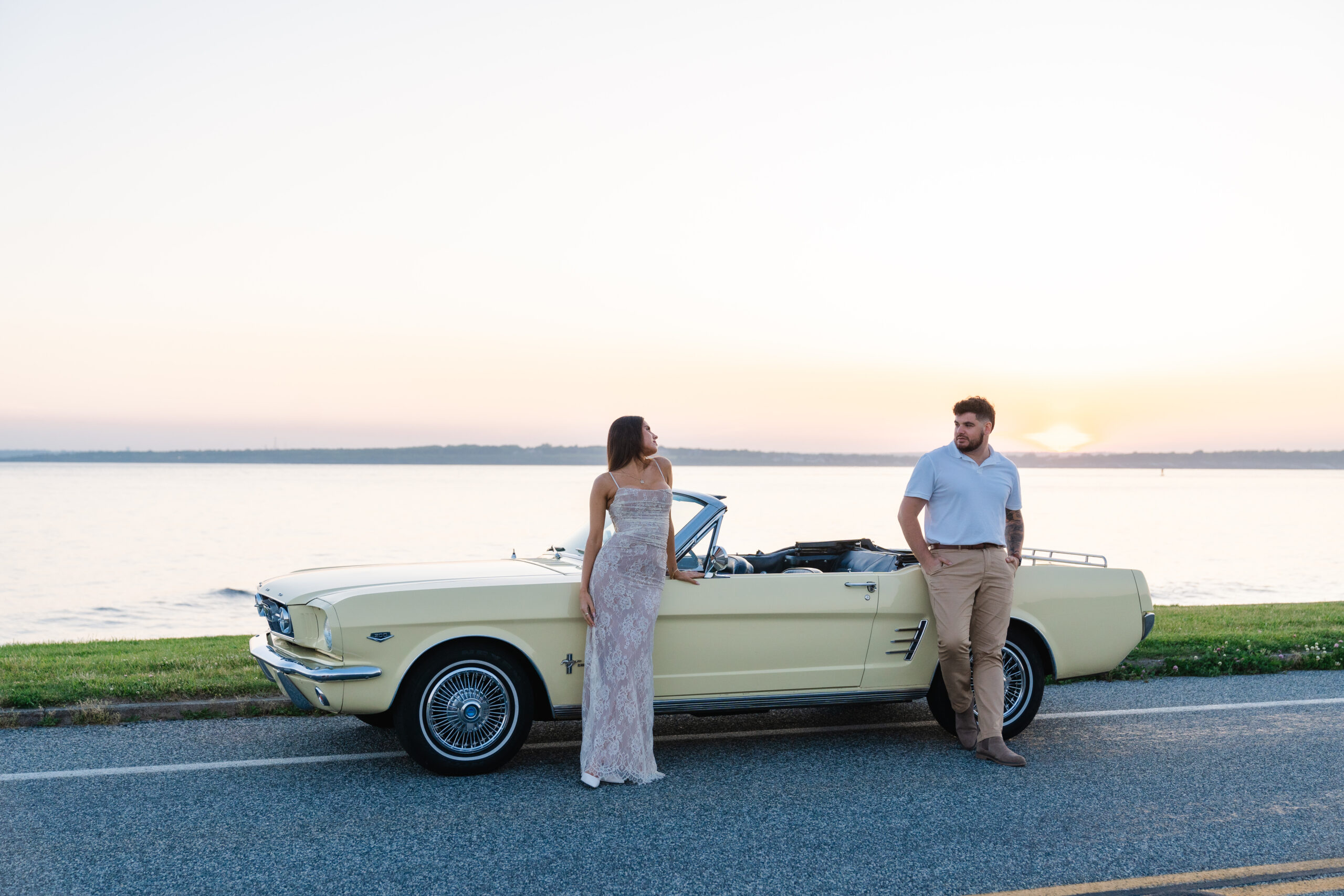 Newly engaged couple smiling at eachother standing in front of a classic car