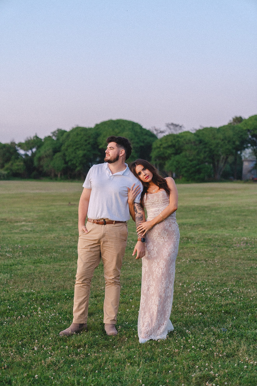 Newly engaged couple posing in a field of grass during sunset