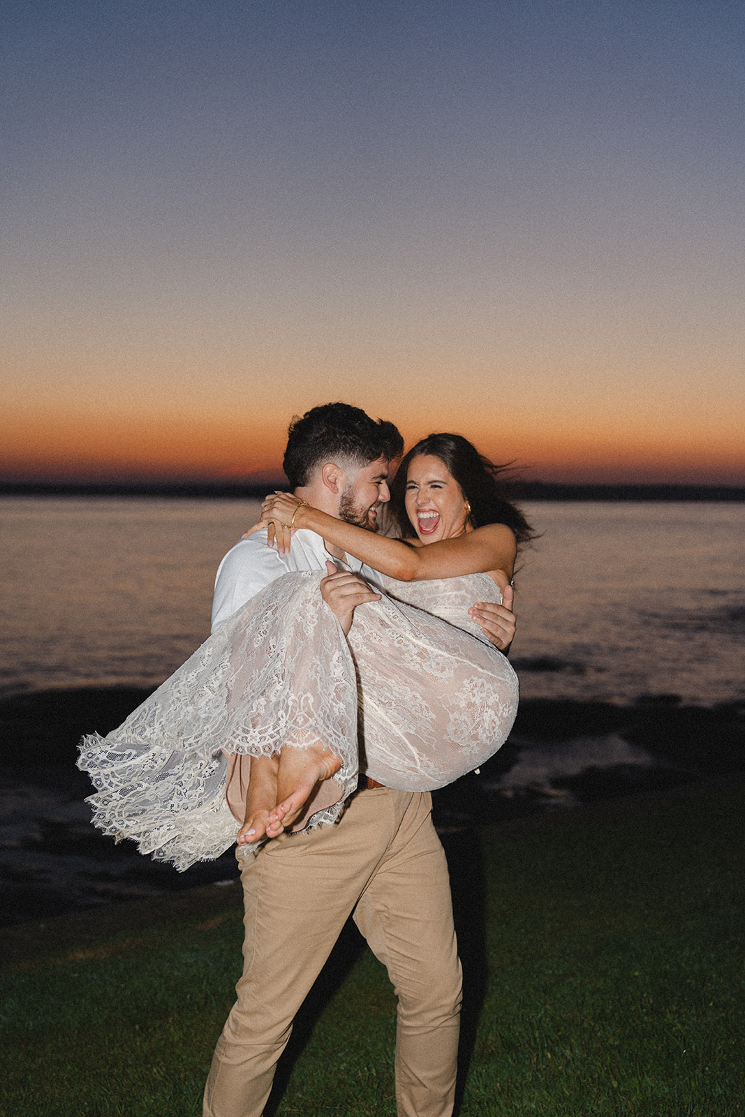 Fiance holding soon to be wife up in the air as she screams with joy during sunset