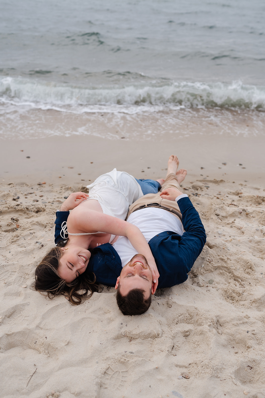 Engaged couple rolling around in the sand at Cape Cod