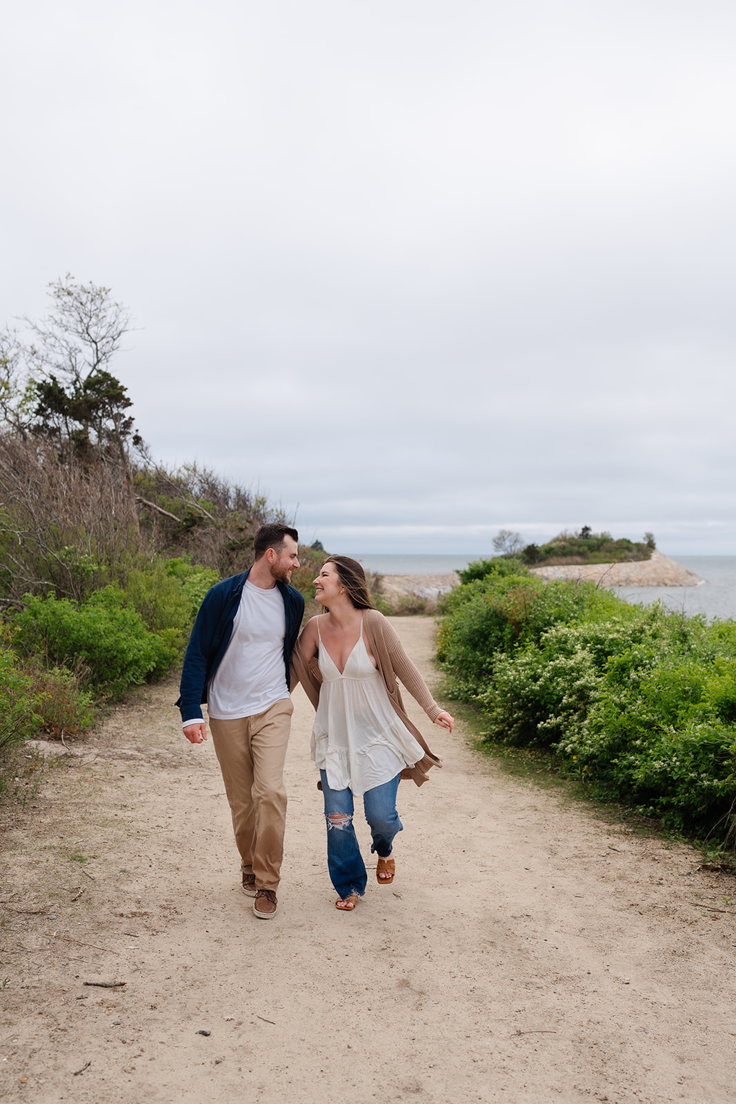 Engaged couple walking holding hands laughing on a dirt road in Cape Cod