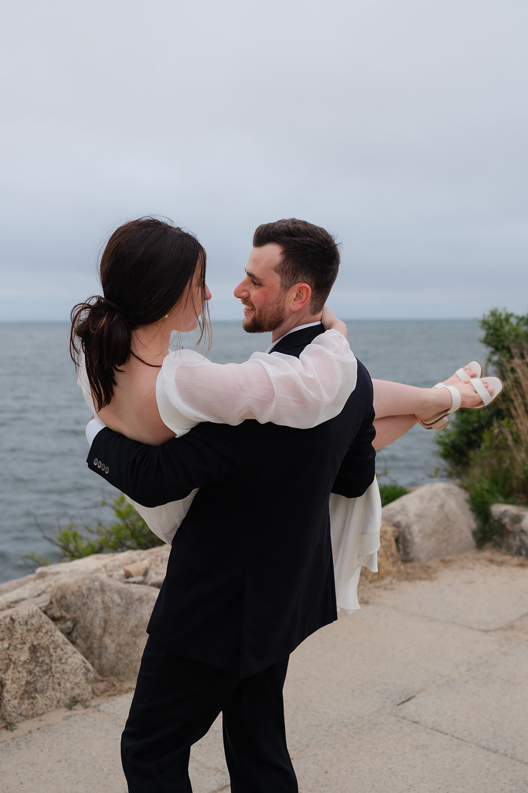 Fiance holding up his soon to be wife smiling at The Knob in Cape Cod