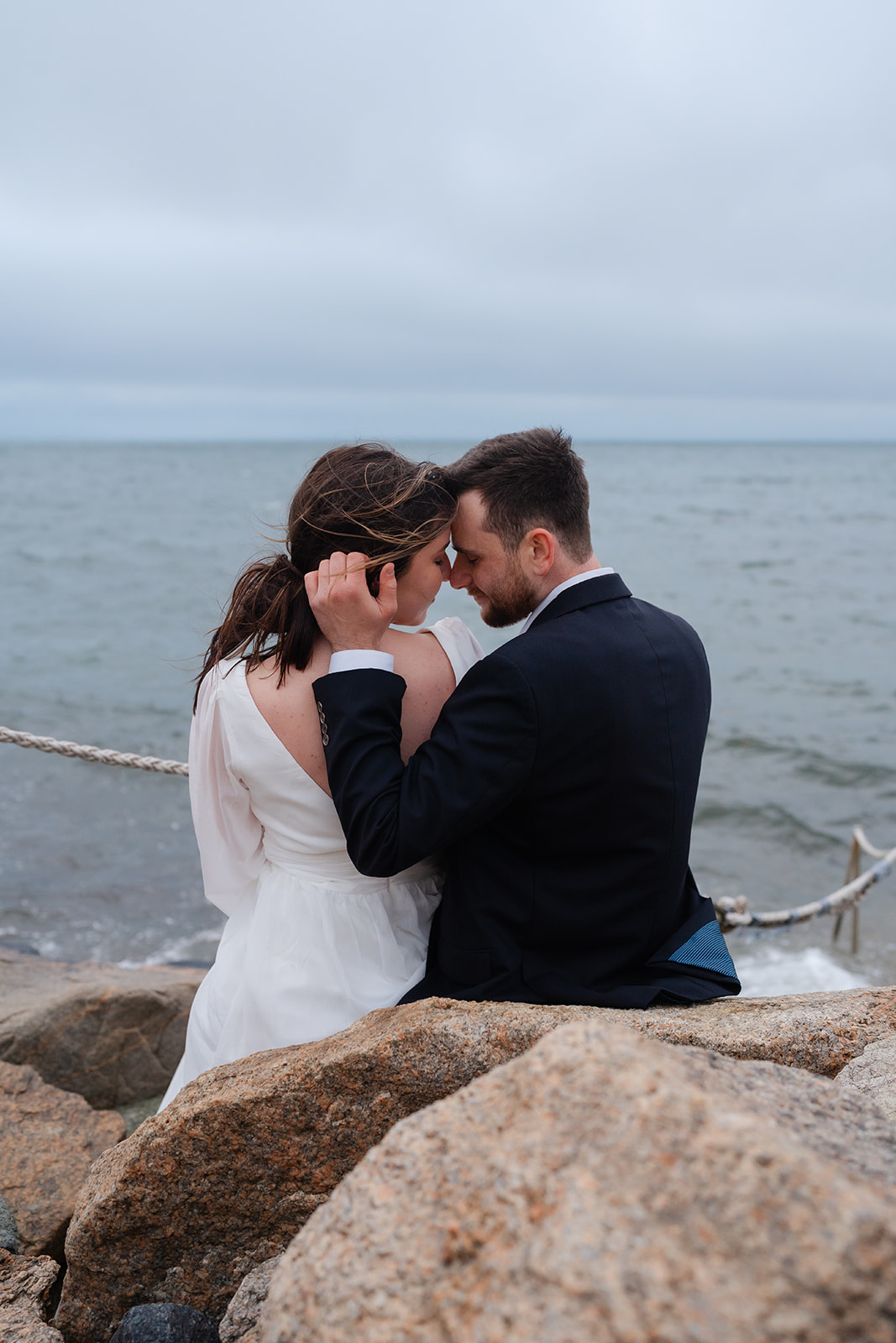 Engaged couple holding eachothers faces looking into eachothers eyes at The Knob in Cape Cod