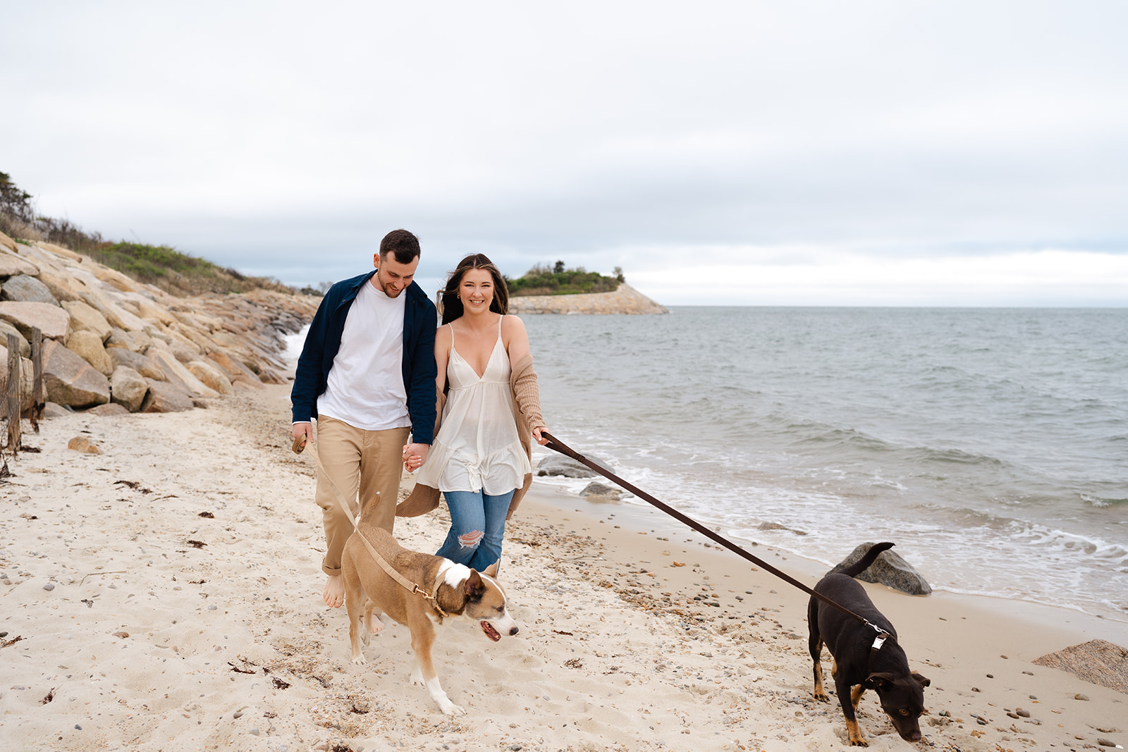 Engaged couple walking their dogs on the beach at Cape Cod