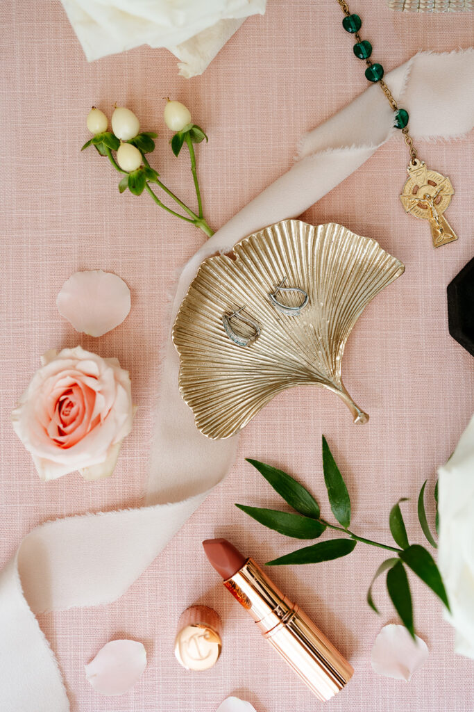 A pink background for a flay lay of the bride's items, her earrings, lipstick and necklace with pink roses around