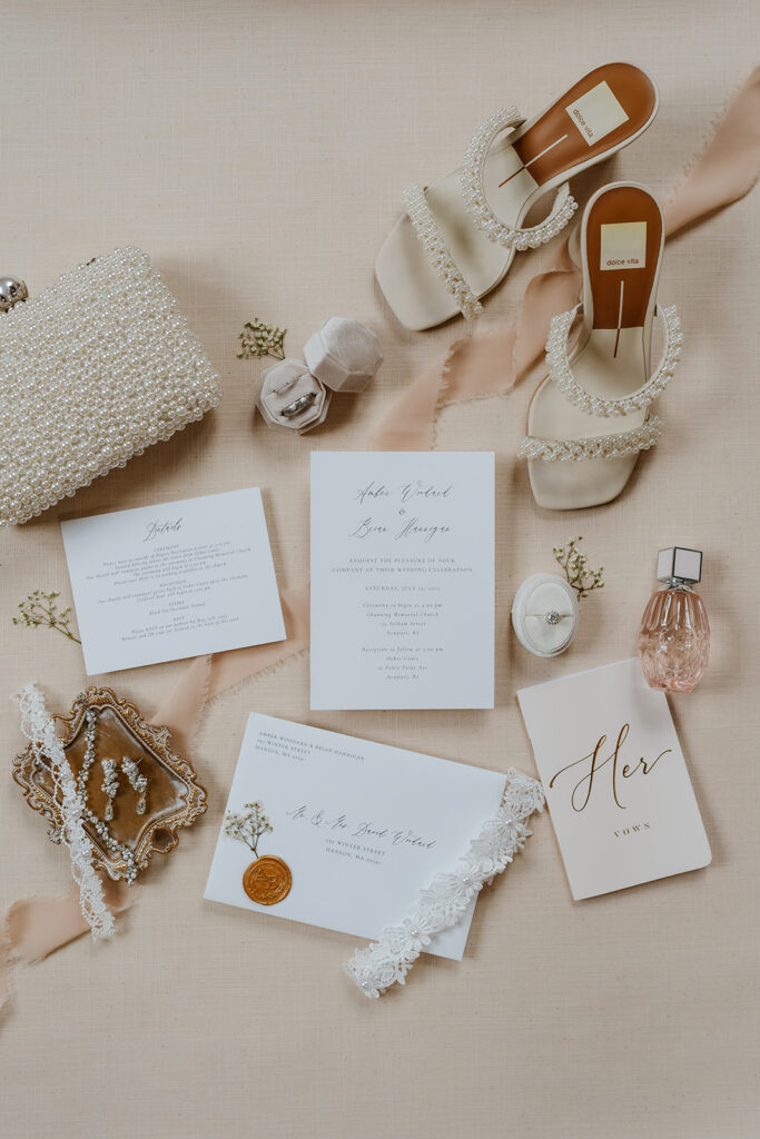 Gorgeous beige theme flay lay of the bride's items, her pearl shoes, pearl clutch, her perfume and her earrings, with all the wedding invitation suite