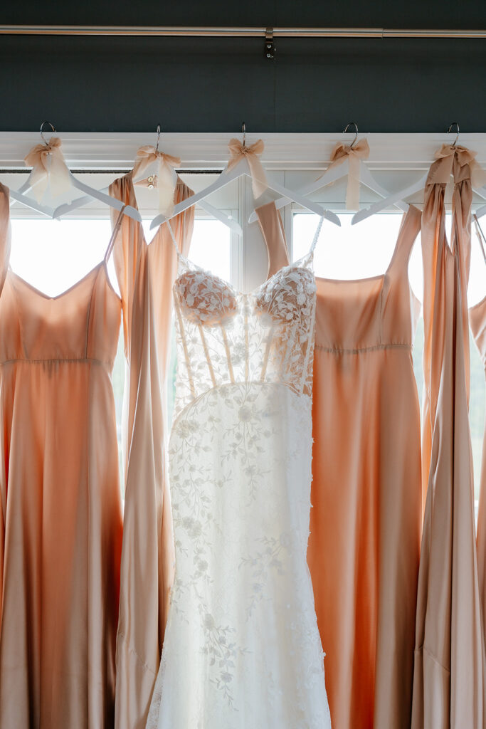 bride's wedding dress with bridesmaids dresses hanging against the window