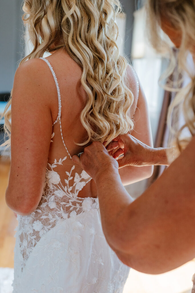 mother of the bride helping put on the bride's wedding dress