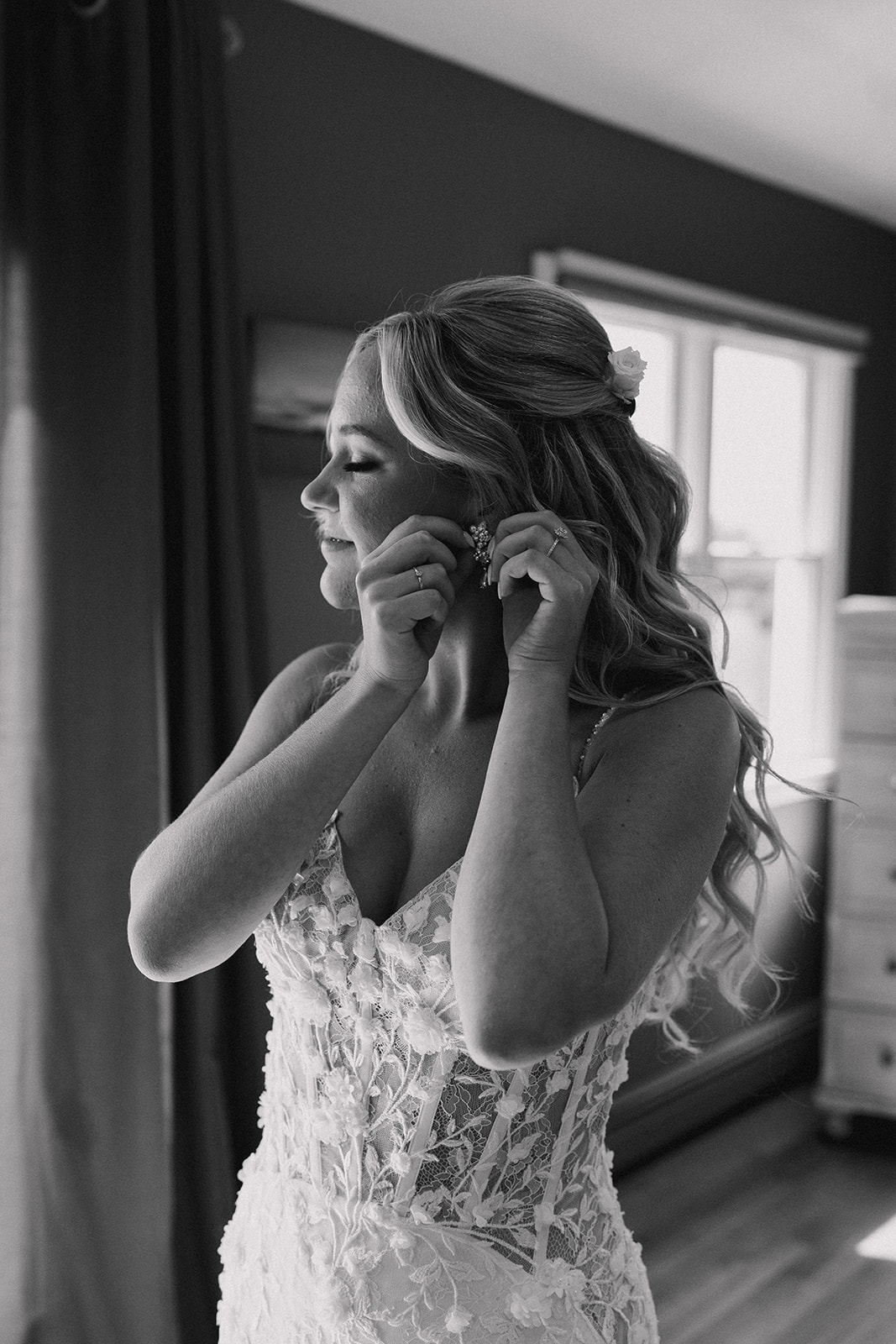 black and white photo of the bride putting her earrings on 