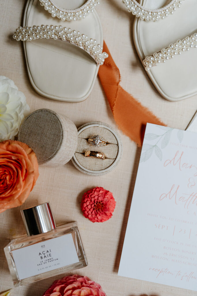 Close up flat flay of the bride's rings, perfume and pearl heels with orange flowers