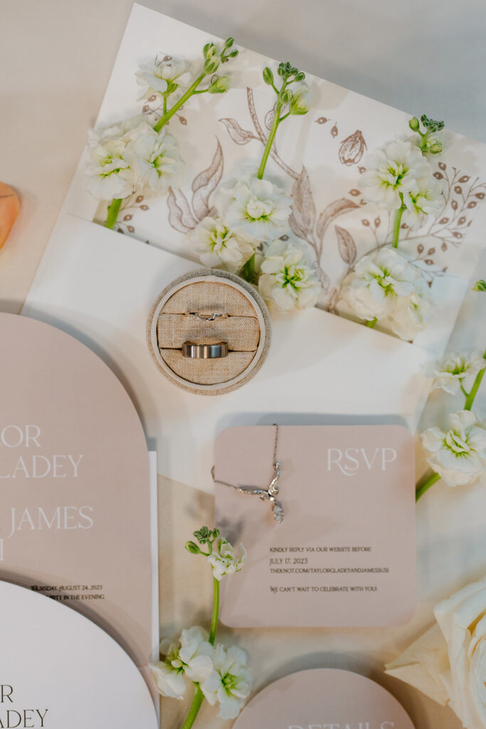 Wedding detailed photo of wedding invitation suite, rings, necklace, with white flowers 