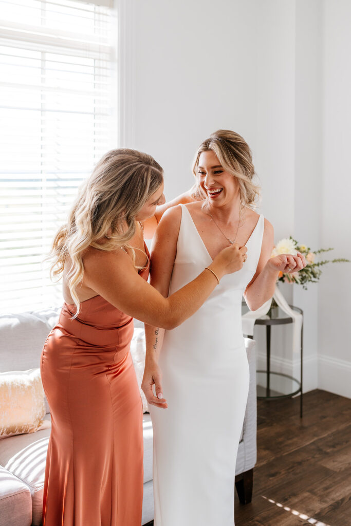 maid of honour helping the bride put on her necklace