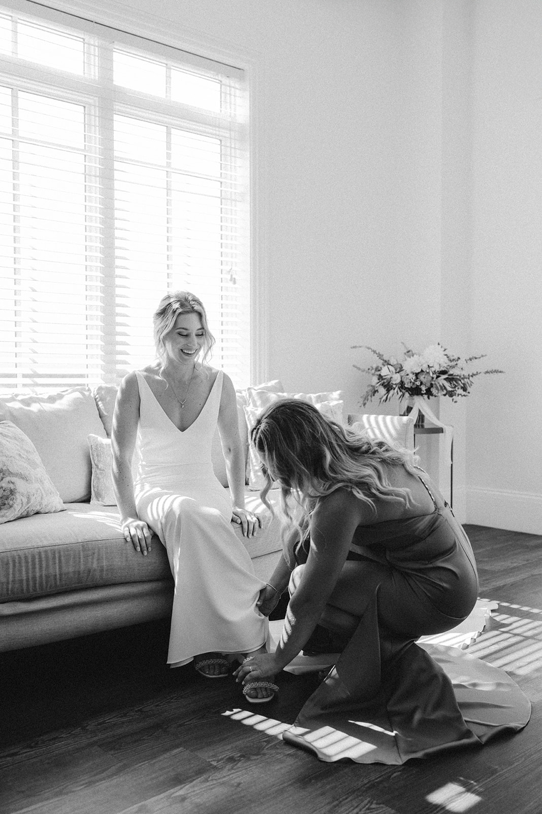 A black and white photo of the bridesmaid helping the bride put on her shoe