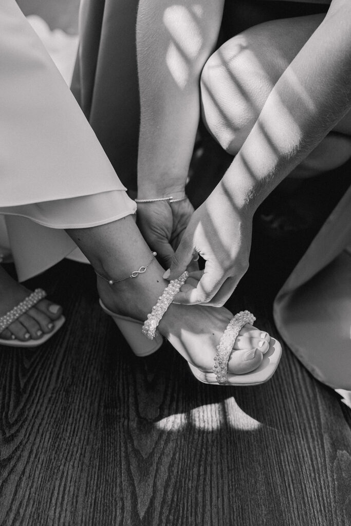 detailed wedding photo of the bridesmaid helping the bride put on her pearl shoe