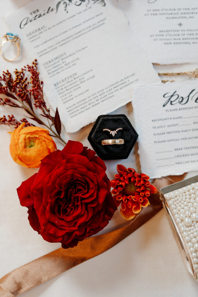 Flat lay of the full invitation suite: RSVP and timeline of the wedding day with red and orange flowers 
