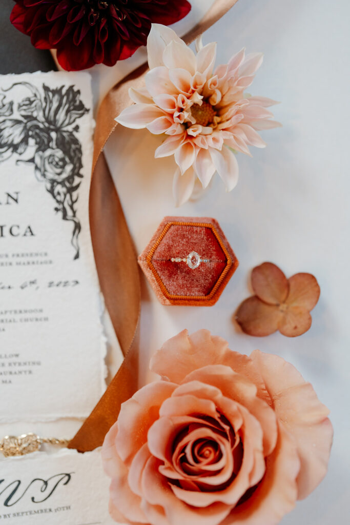 Orange theme wedding detail photo of the wedding ring next to wedding invitation card with orange flowers around