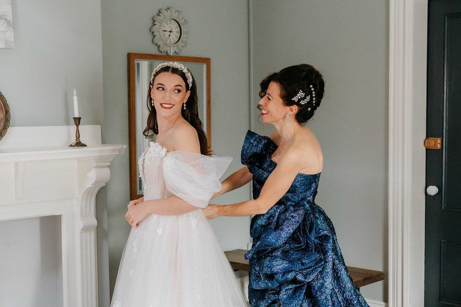 mother of the bride helping the bride put on her dress, smiling